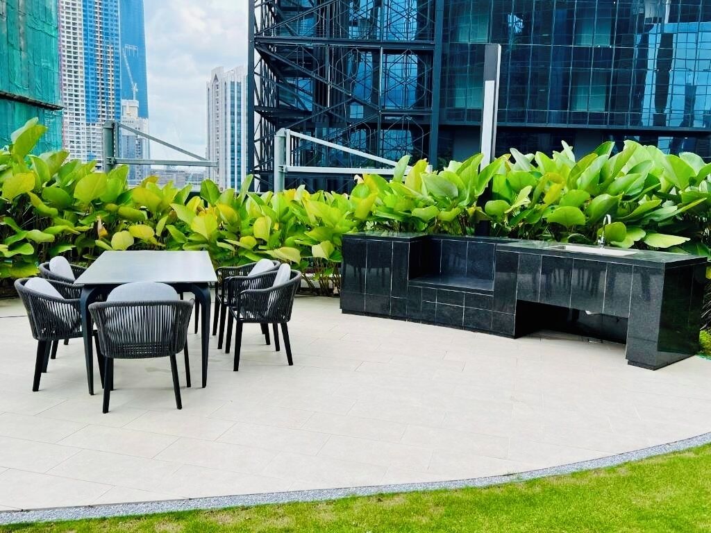 Et udendørs siddeområde i moderne stil, med et sort møbelarrangement bestående af borde og stole, omgivet af frodige, grønne planter.