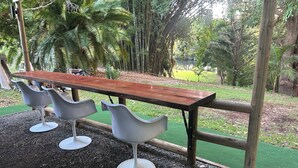 A wooden bench with a metal frame, surrounded by three white bar stools. - The Bello BigRig - Luxury Riverfront Bus Conversion, close to town, pet friendly (Bellingen)