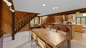 Eine geräumige Küche mit einer Holztreppe, einem Essbereich mit großem Tisch und Stühlen sowie Blick ins Freie durch die Fenster.