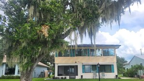 A two-story house with a large tree in the front yard.