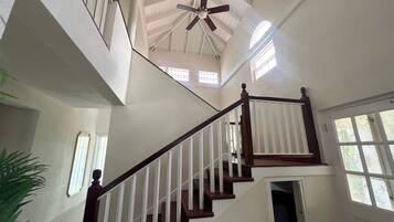A multi-level interior with a central staircase, a ceiling fan, and windows allowing natural light.