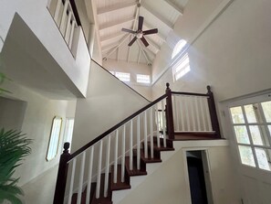A multi-level interior with a central staircase, a ceiling fan, and windows allowing natural light. - Jack's Place - by Zenbreak (Mullins)