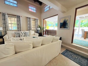 A spacious living room with a large sofa, multiple windows, and a view of the outdoors. - Jack's Place - by Zenbreak (Mullins)