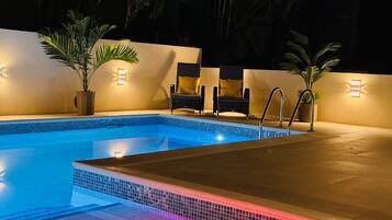 A swimming pool with a tiled edge, surrounded by walls with built-in lighting, and two potted plants.