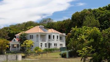 A large white building with multiple windows and a red roof, surrounded by lush greenery.