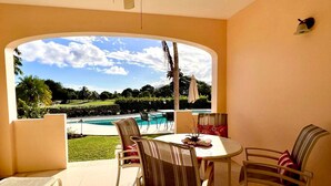 A patio with a table and chairs, a ceiling fan, and a view of a swimming pool and greenery. - Island Time El Sol - by Zenbreak (Durants)