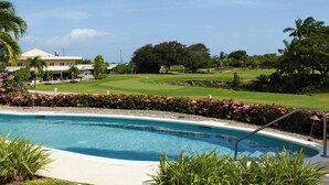 A swimming pool with a view of a golf course and a building in the background. - Island Time El Sol - by Zenbreak (Durants)
