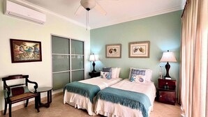 A bedroom with two beds, a ceiling fan, a window with frosted glass, a chair, a nightstand, and a lamp. - Island Time El Sol - by Zenbreak (Durants)
