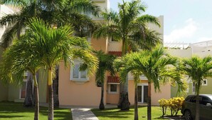 A building with a paved walkway, palm trees, and a parked car. - Island Time El Sol - by Zenbreak (Durants)