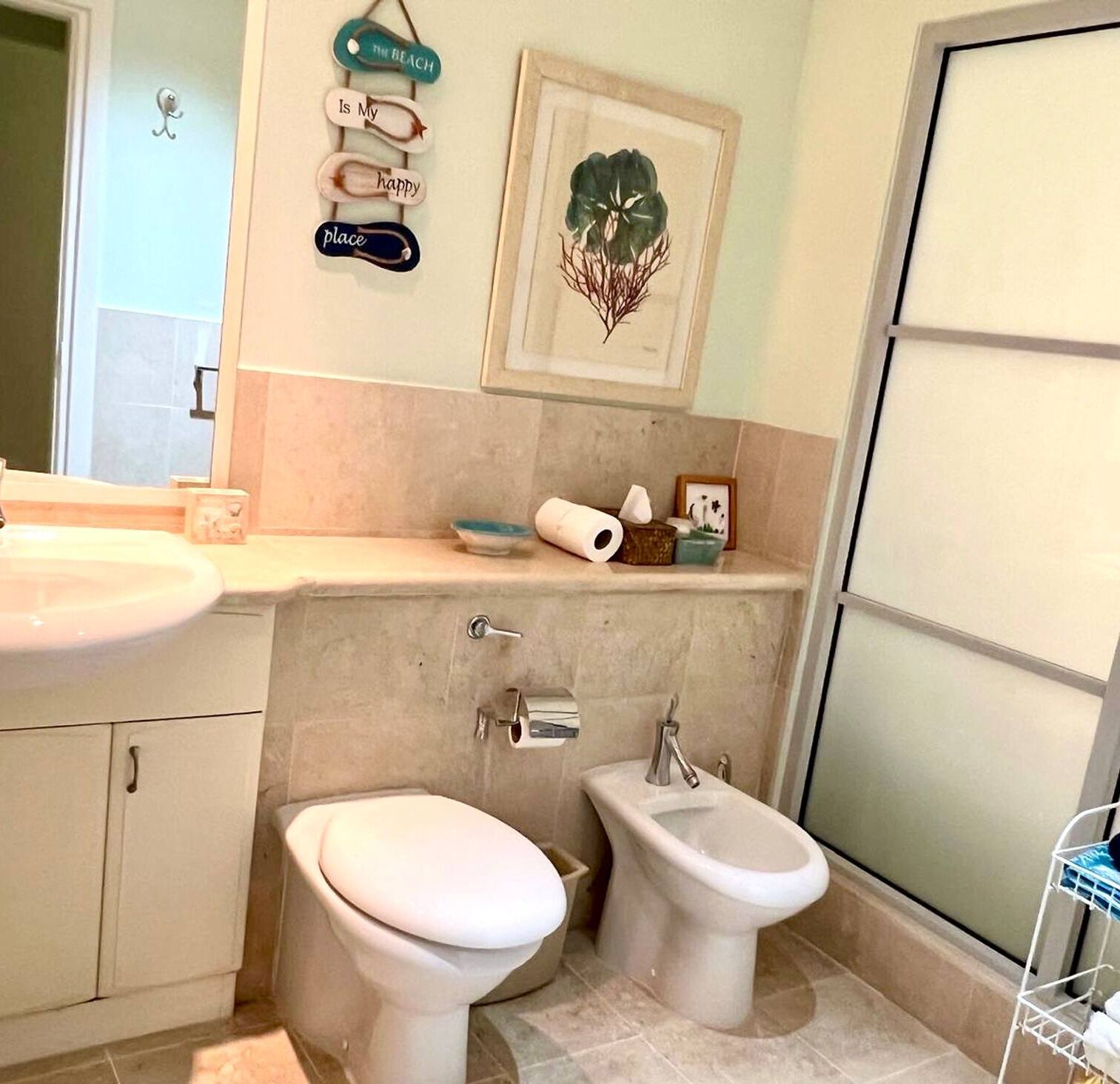 A bathroom with a toilet, bidet, sink, and a small shelf with toiletries.