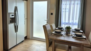 Une cuisine compacte équipée d’un réfrigérateur, d’une table à manger avec des assiettes et un verre à vin, et d’une fenêtre avec des rideaux.