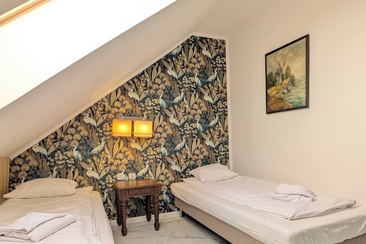 A bedroom with two beds, a nightstand, a lamp, and a painting on the wall.
