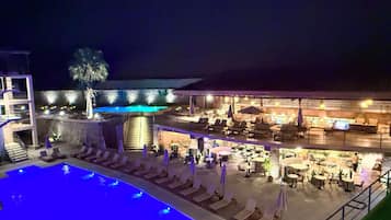 A nighttime view of a hotel with a swimming pool, outdoor seating, and a bar area.