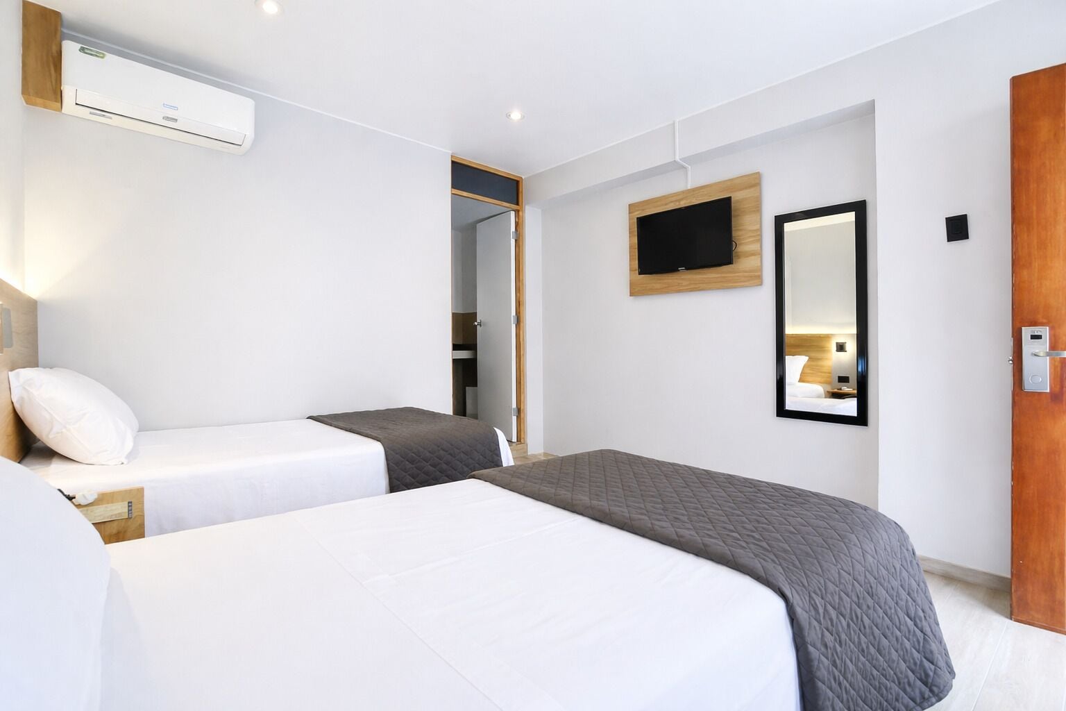 Et hotelværelse med to senge, et fjernsyn, et spejl og en aircondition.