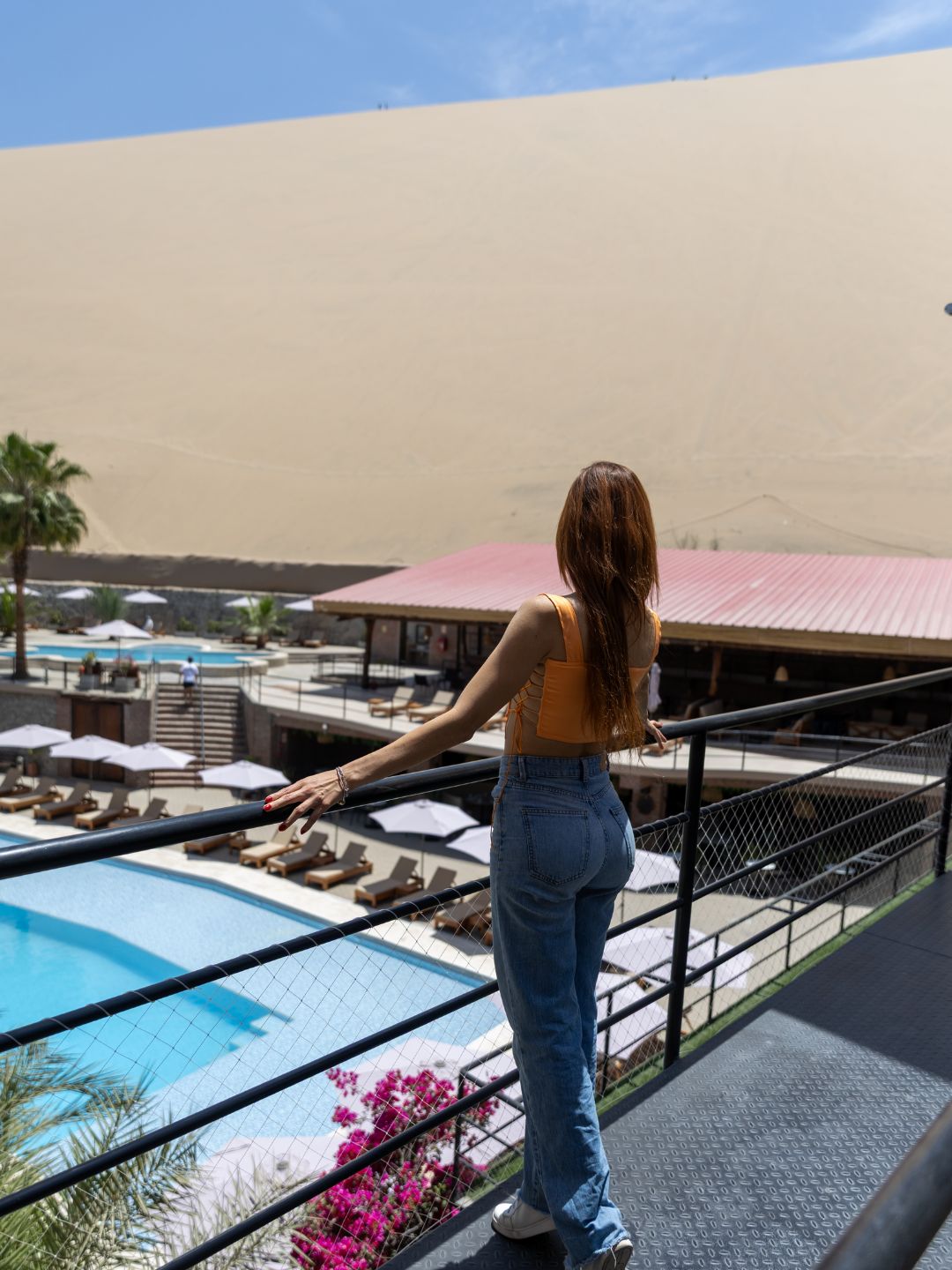 A person overlooking a pool area with lounge chairs and a desert landscape in the background.