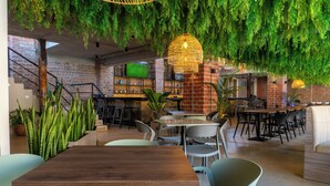 Un restaurante moderno con paredes de ladrillo, plantas colgantes verdes y diferentes opciones de asientos, incluyendo mesas y sillas.