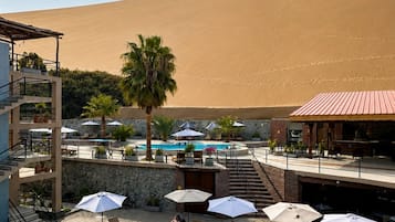 Ein Poolbereich mit Liegestühlen und Sonnenschirmen, eine Treppe, die zu einem Gebäude führt, und eine Wüstenlandschaft im Hintergrund.
