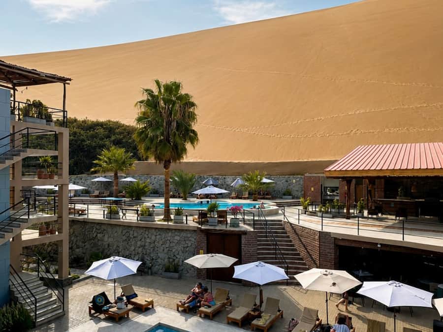 Zona de piscina amb gandules i ombrelles, una escala que condueix a un edifici i un paisatge desertànic al fons.