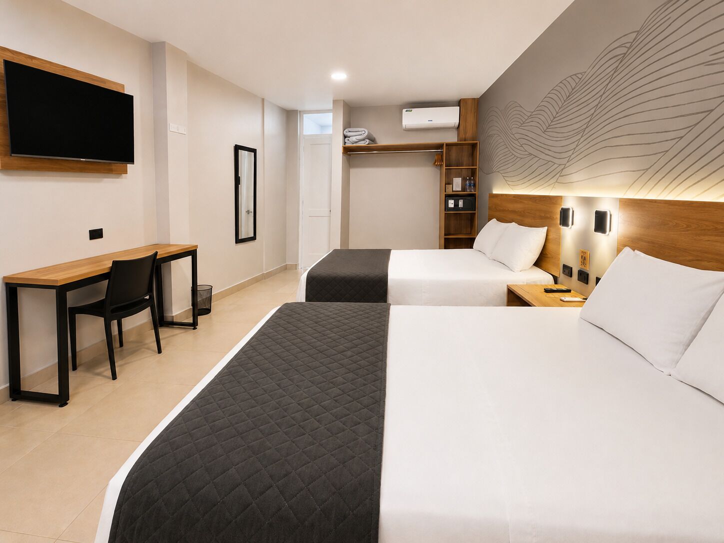 A hotel room with a desk, two beds, a TV, and a wall-mounted air conditioner.