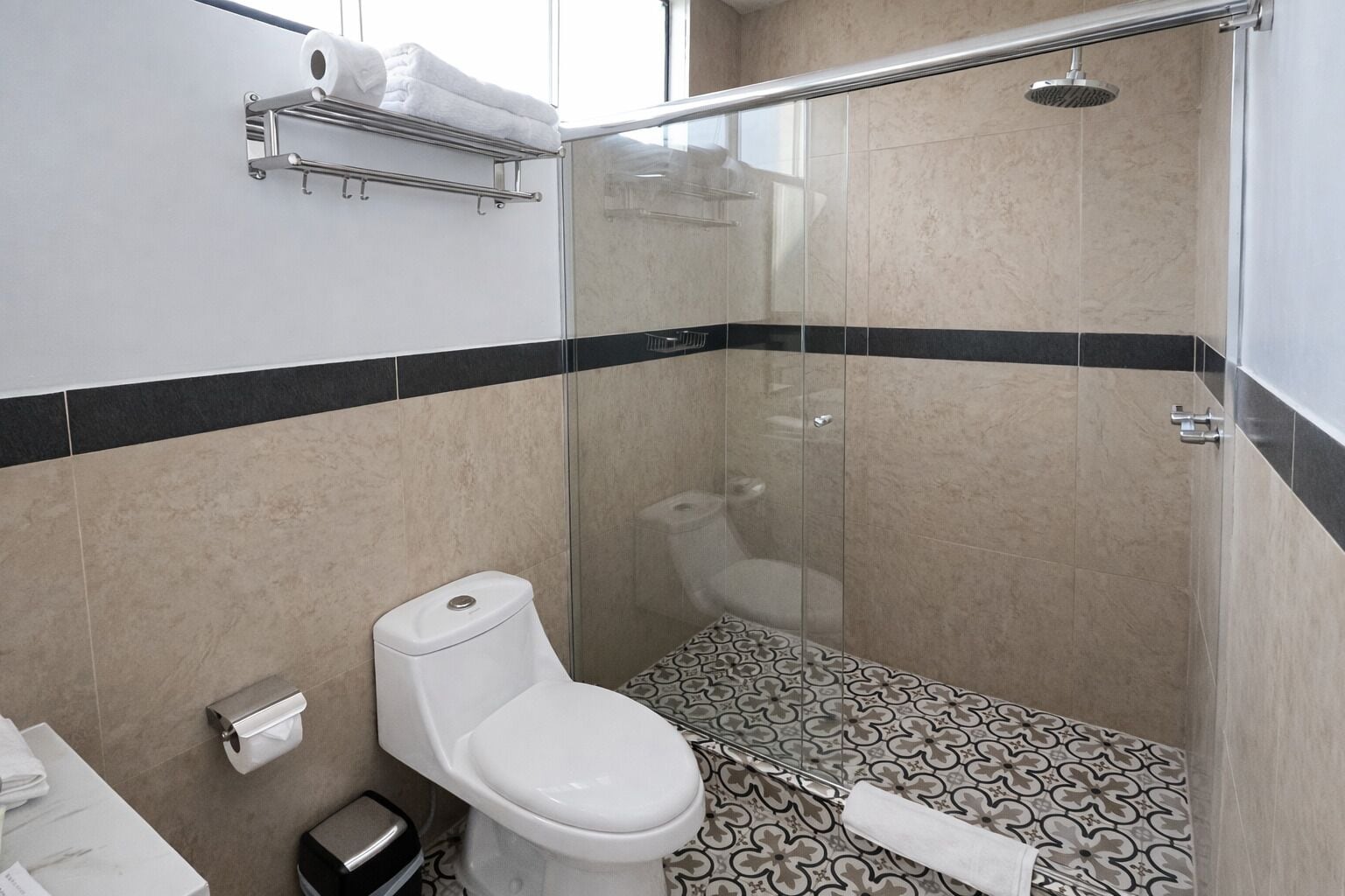 A modern bathroom with a toilet, shower, and patterned floor tiles.
