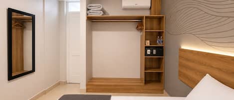 Habitación de hotel con cama, armario, espejo, estante con artículos de aseo y aire acondicionado de pared.
