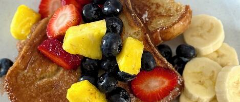 A plate of French toast topped with sliced bananas, strawberries, blueberries, and pineapple chunks.