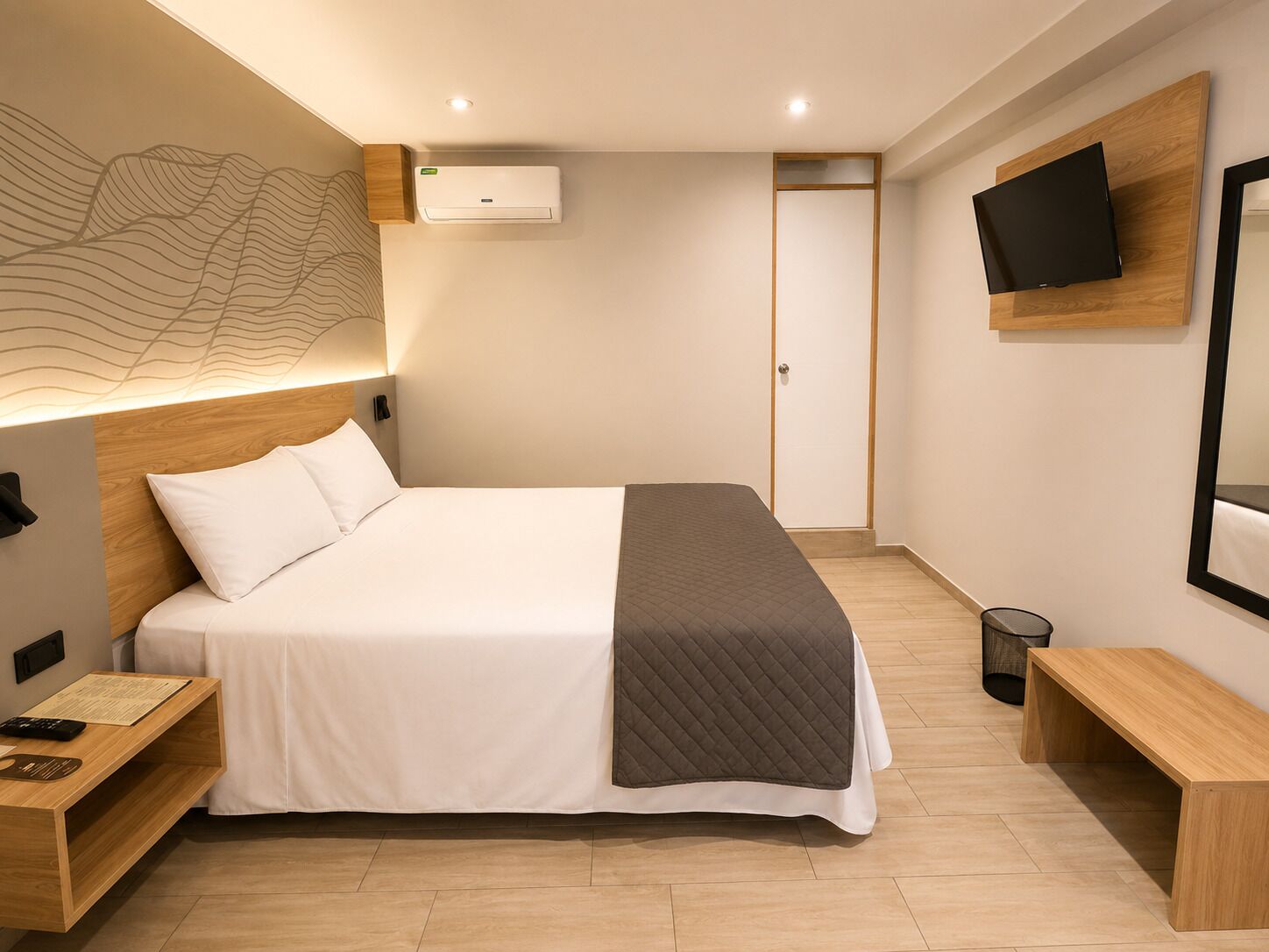 Habitación de hotel moderna con una cama grande, mesitas de noche, un televisor de pantalla plana y un aire acondicionado de pared.