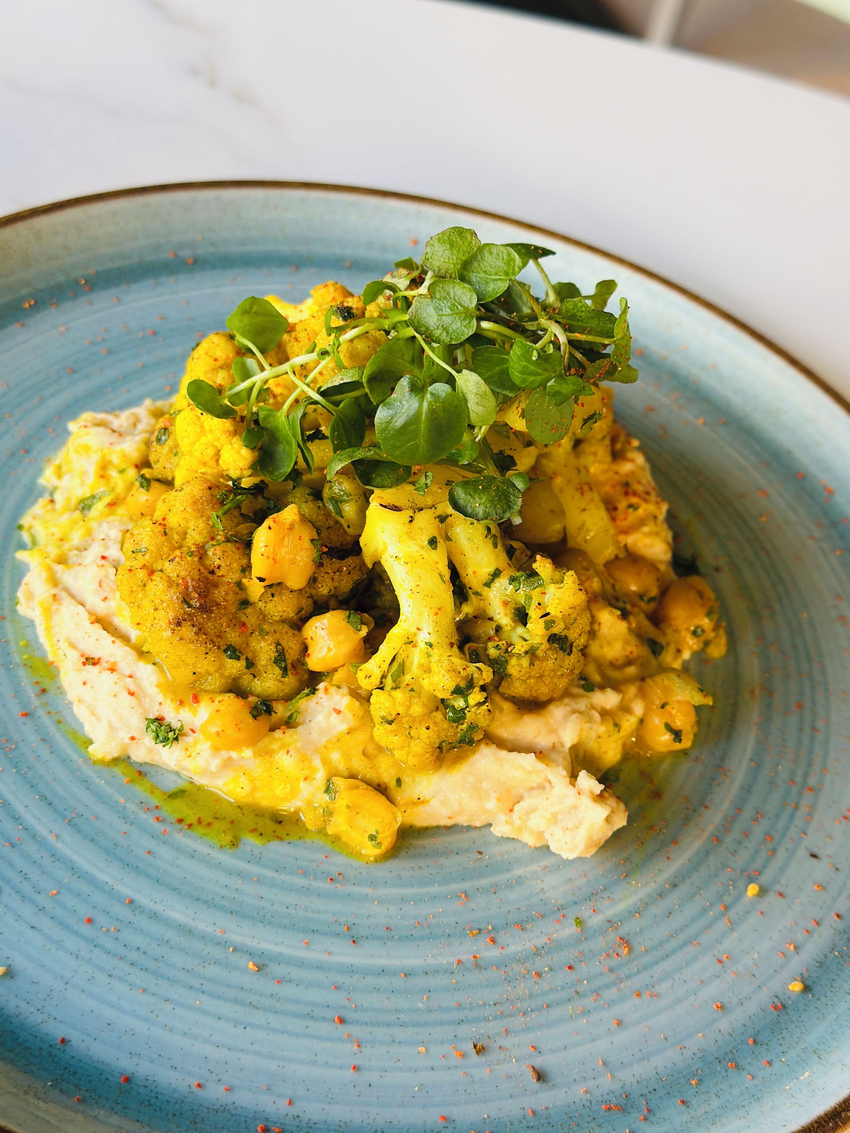 A plate of food with cauliflower, chickpeas, and a garnish of microgreens.