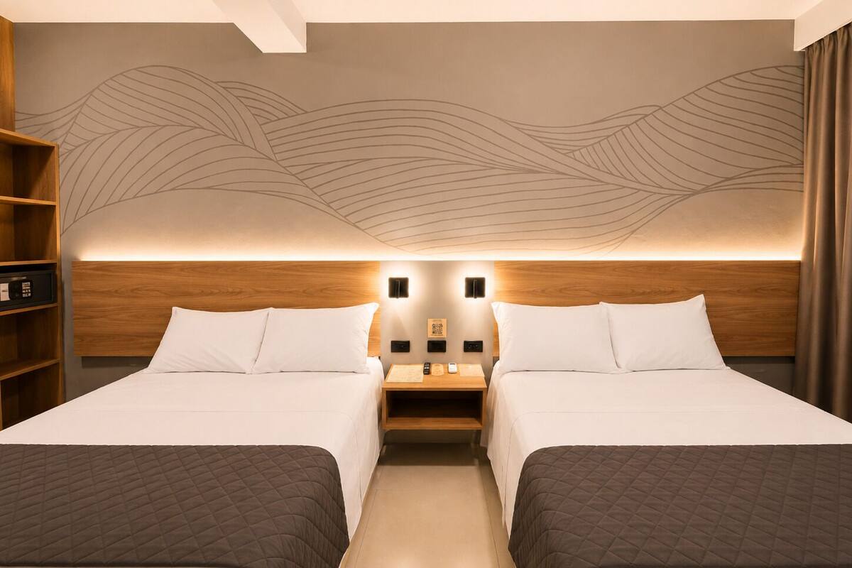 A hotel room with two beds, a wooden headboard, a wall mural, bedside tables, and a bookshelf.