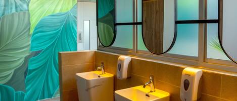 A modern bathroom with two sinks, a mirror, and a hand soap dispenser.