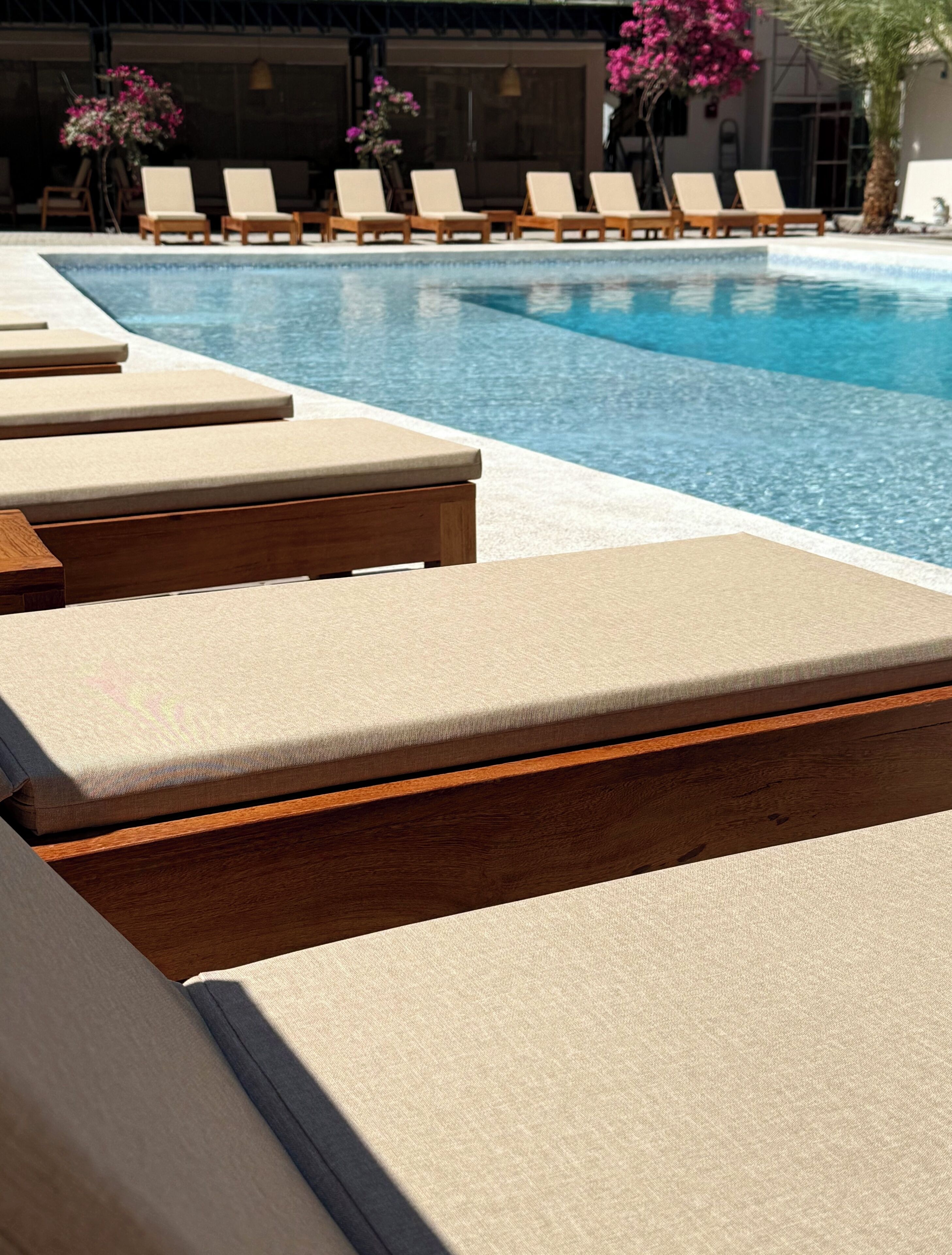 Un área junto a la piscina con sillones de madera y una piscina azul cristalina.