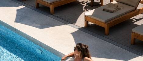 A poolside area with lounge chairs and a person sitting by the pool.