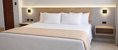 Una cama bien hecha con ropa blanca y un plaid color beige, flanqueada por dos mesitas de noche con iluminación integrada, en una habitación de hotel moderna.