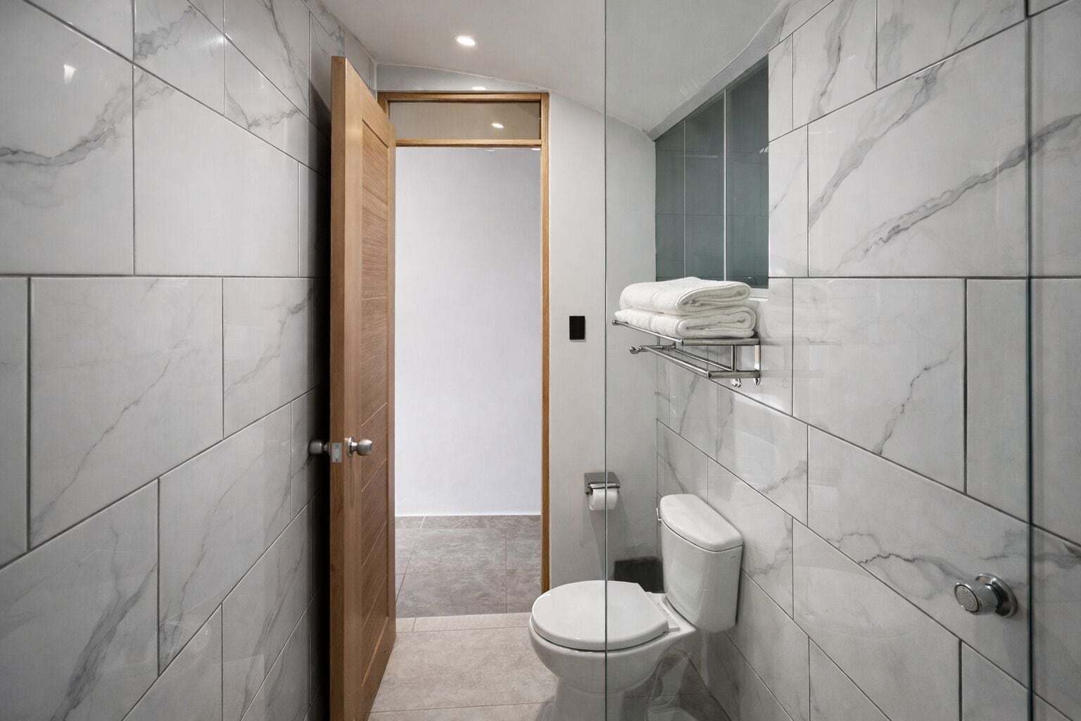 A modern bathroom with marble tiles, a toilet, a towel rack, and a wooden door.