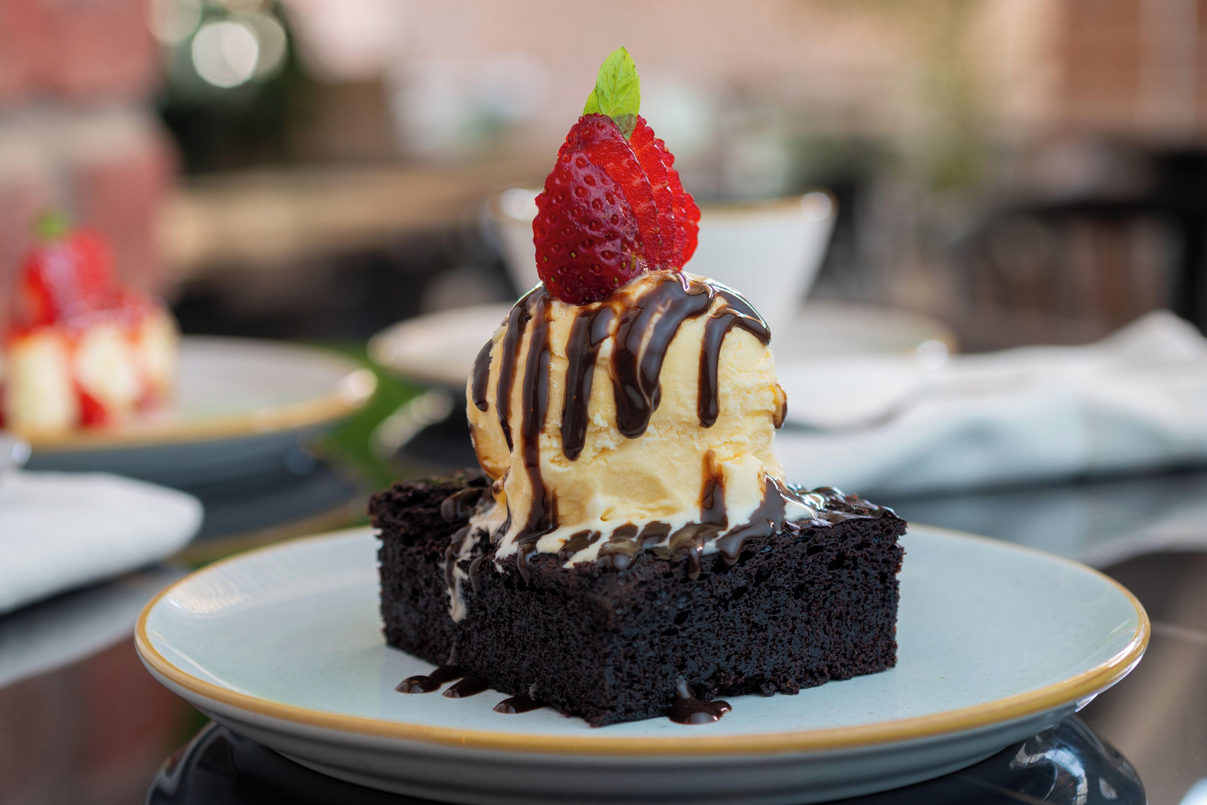 Un postre en un plato con base de chocolate, cubierto de helado y una fresa, y rociado con salsa de chocolate.