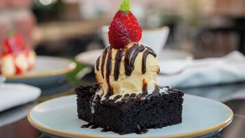 Un postre en un plato con base de chocolate, cubierto de helado y una fresa, y rociado con salsa de chocolate.