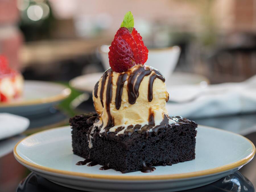 Un postre en un plato con base de chocolate, cubierto de helado y una fresa, y rociado con salsa de chocolate.