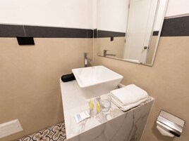 Un baño con lavamanos blanco, espejo y toallero.