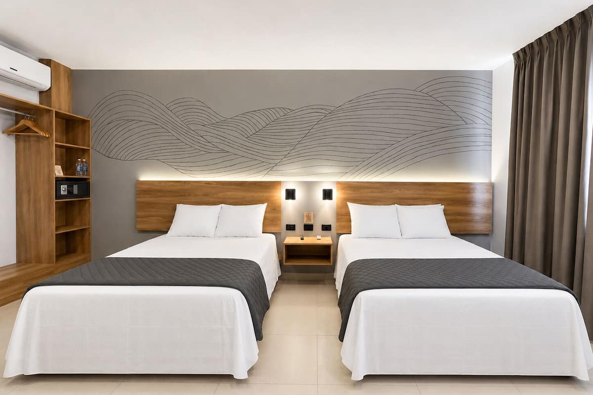 A hotel room with two beds, a wooden headboard, a wall-mounted shelf, and a large abstract mural.