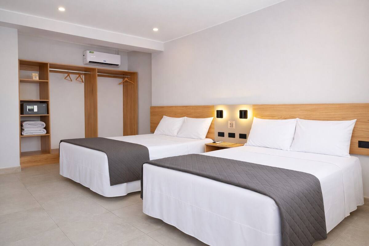 A hotel room with two beds, a wardrobe, and a wall-mounted air conditioning unit.