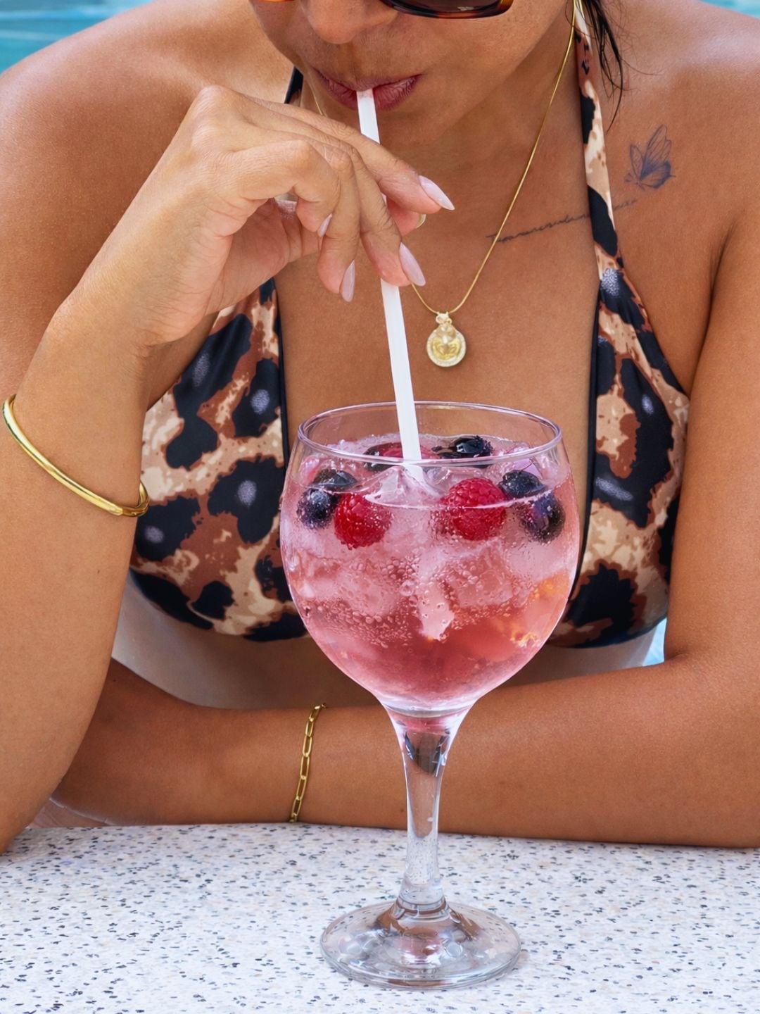 A person in a patterned swimsuit sitting at a table with a glass of iced beverage containing berries.