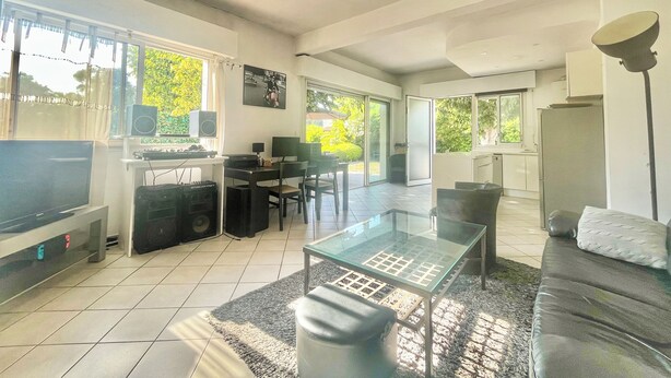 A modern living room with a flat-screen TV, a glass coffee table, a sofa, and a dining area with a table and chairs.