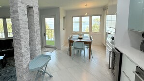 Une cuisine moderne avec des meubles blancs, un mur d’accent en pierre et un coin repas comprenant une table et des chaises.
