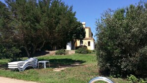 A poolside area with a clear view of a building in the background, surrounded by greenery. - Villa Sirenetta - Punta De Su Tu... (Punta de su turrione)