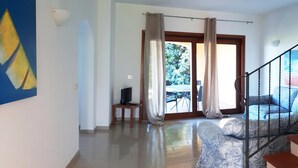 A spacious room with a bed, a TV on a small table, a staircase, and a view of the outdoors. - Villa Sirenetta - Punta De Su Tu... (Punta de su turrione)