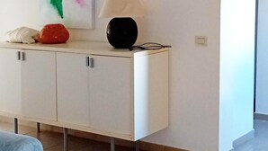 A room with a white cabinet, a painting, a lamp, and a red object on top. - Villa Sirenetta - Punta De Su Tu... (Punta de su turrione)