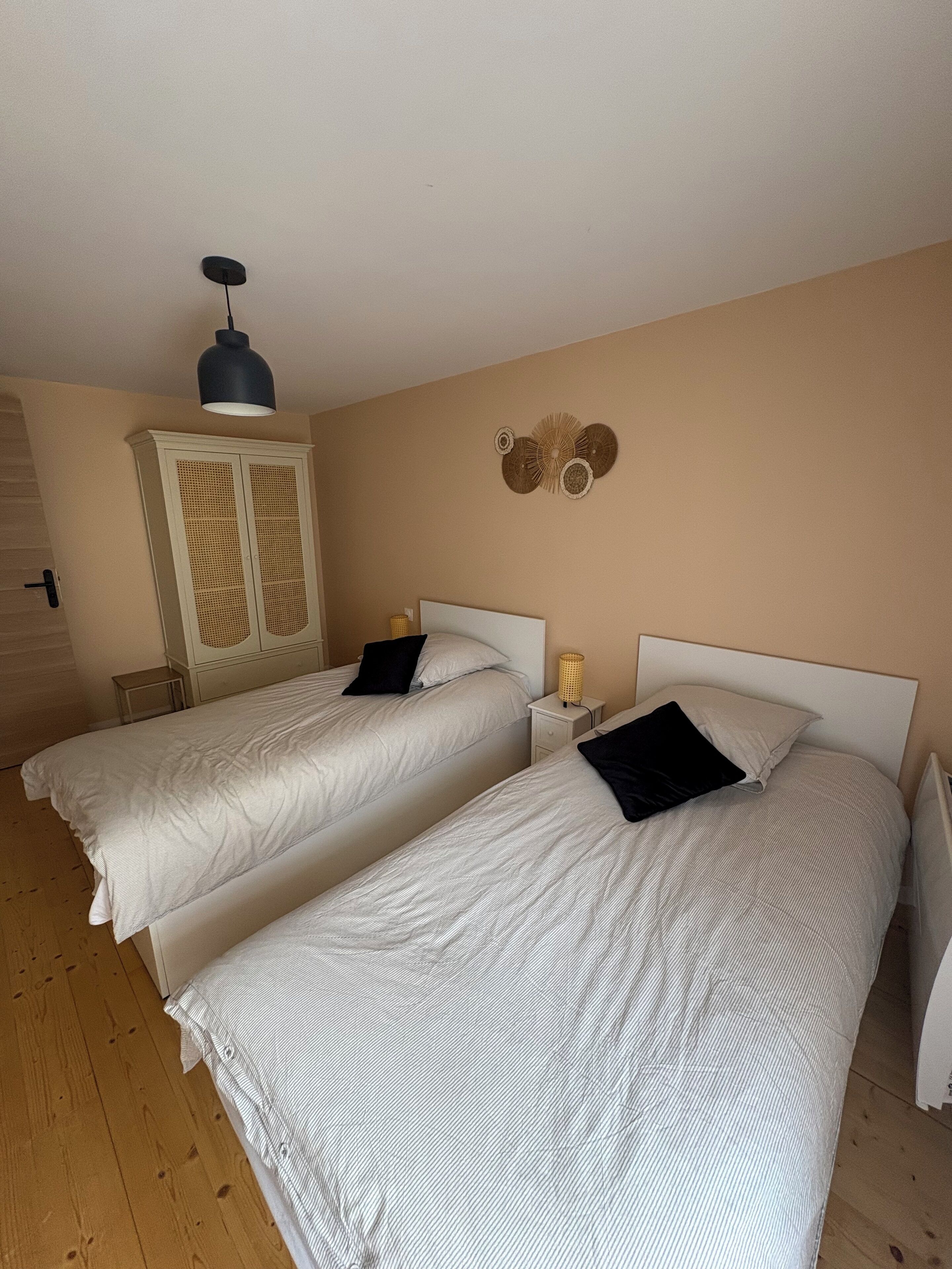 A hotel room with two single beds, a wardrobe, a lamp, and a wall decoration.