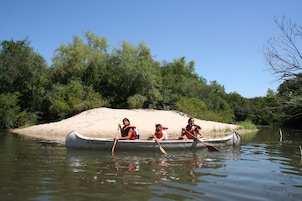 Uma canoa com três pessoas remando em um rio rodeado por árvores.
