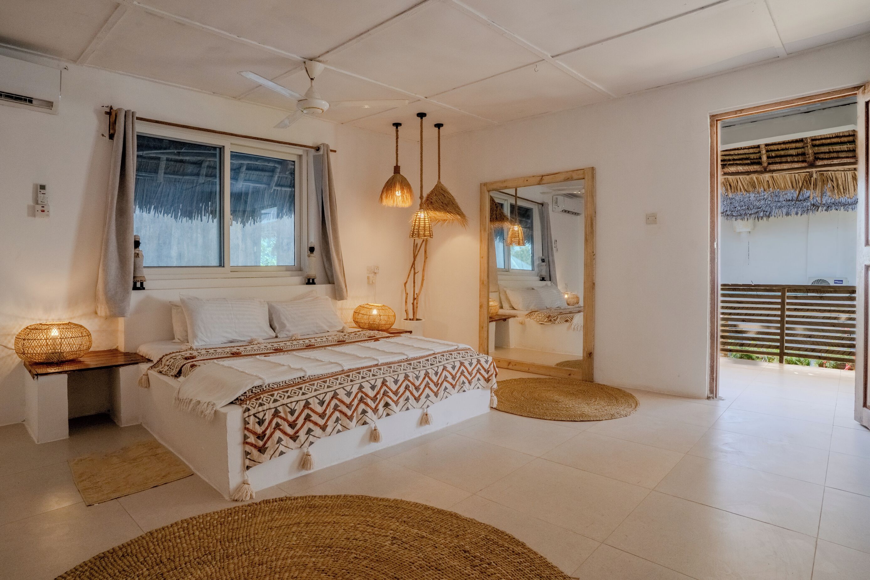 A bedroom with a bed, bedside lamps, a mirror, and a view of the outdoors.