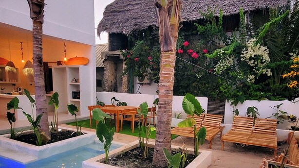 Un espace piscine agrémenté d’une structure à toit de chaume, de mobilier en bois et de plantes tropicales.